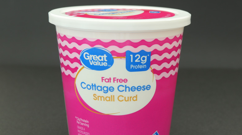 Pink plastic tub of Great Value fat free small curd cottage cheese on gray background