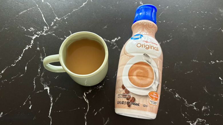 Bottle of Great Value brand original coffee creamer next to pastel green mug of coffee on black marble surface