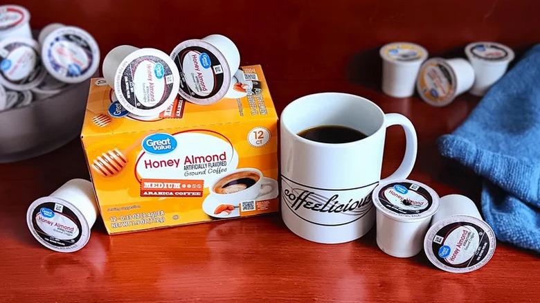 A box of Great Value honey almond coffee pods with pods scatttered beside it, a cup of brewed coffee in the foreground
