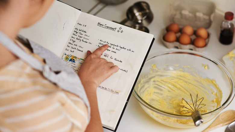 Woman holding open recipe book in kitchen next to bowl of cake batter