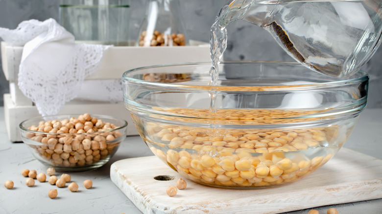 a pitcher of water poured over garbanzo beans in a glass bowl