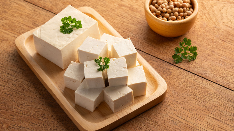 A brick of tofu on a small wooden tray, half of it cut into cubes