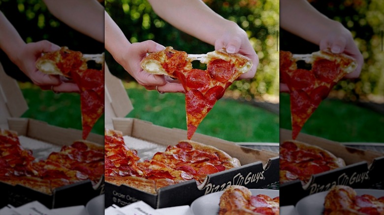 Someone pulling a slice of stuffed-crust pepporini pizza from a Pizza Guys box