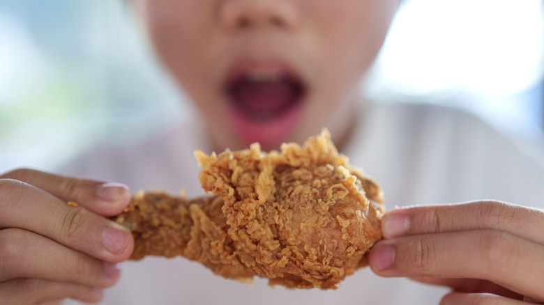 A person holding a piece of fried chicken