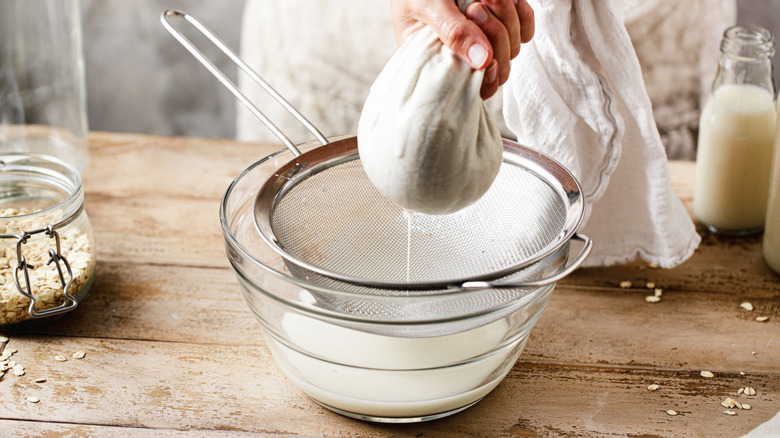 A woman squeezed oat water through a cheesecloth into a bowl
