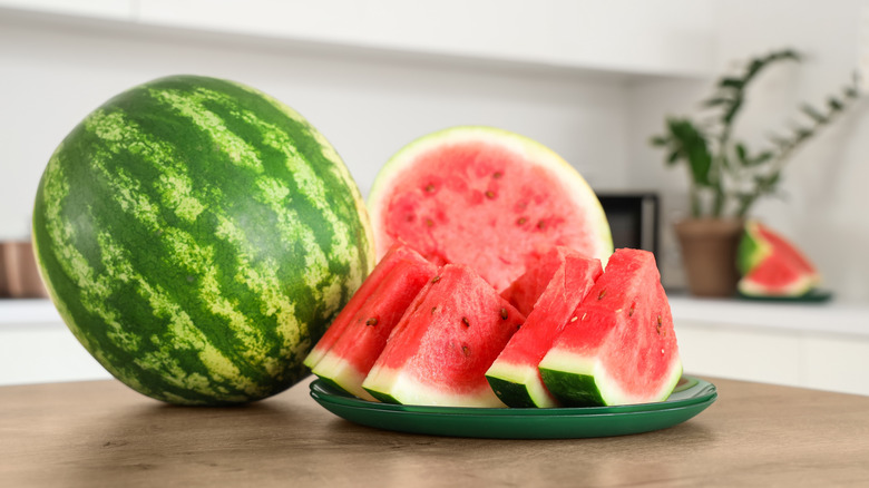 a whole watermelon next to slices on a plate on a wooden countertop