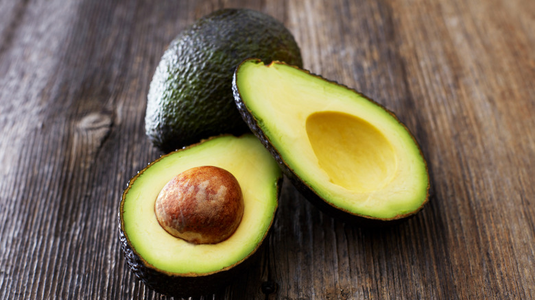 Halved and whole avocados on wooden table