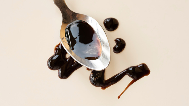 Drizzle of balsamic vinegar on a silver spoon on beige background