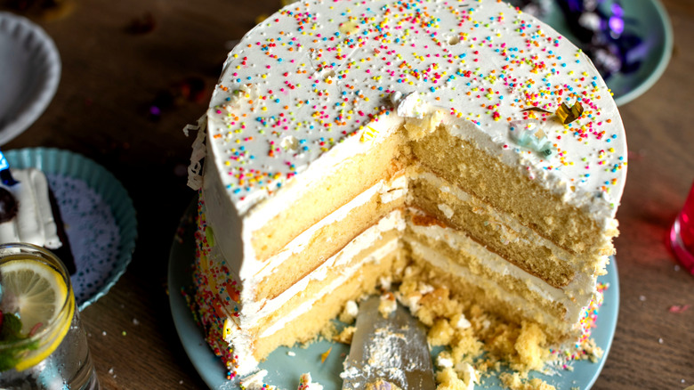 Vanilla layer cake with slice taken out covered with buttercream and colorful sprinkles