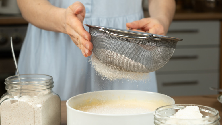 A person's hands sifting flour through a mesh strainer