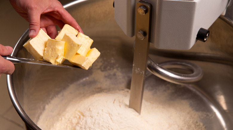 Baker adding butter to the bowl of a commercial-sized floor-standing mixer