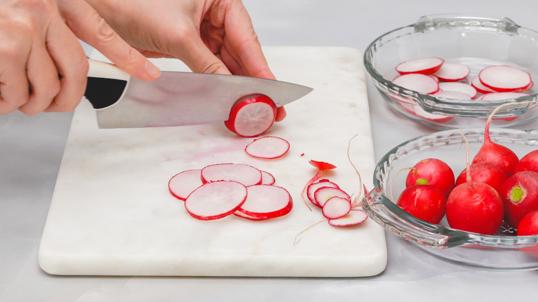 Person slicing radishes on a marble cutting board