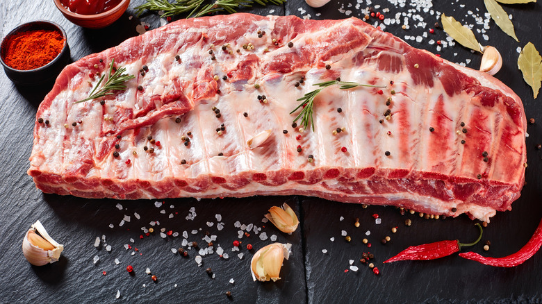 raw slab of pork ribs on board with seasonings
