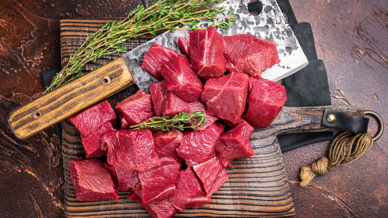 raw meat cut in cubes on board with cleaver