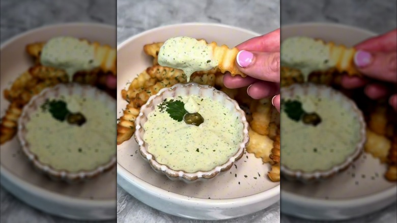 Hand dunking crinkle fries into a bowl of jalapeño mayo