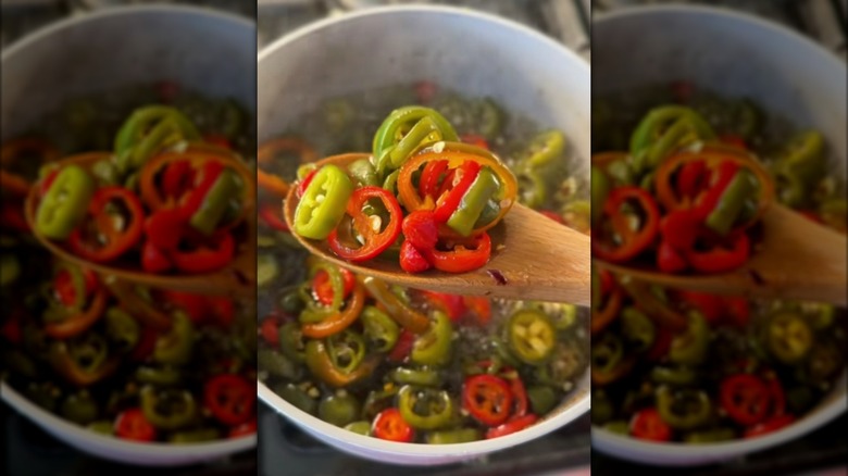 Lifting candied jalapeños from a saucepan with a wooden spoon
