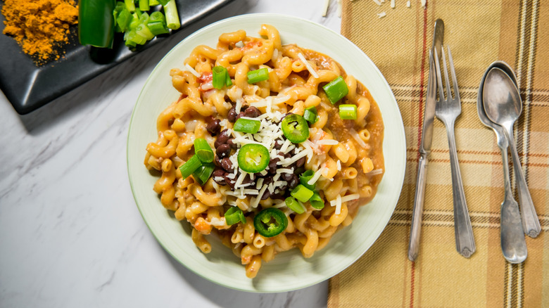 Plate of mac and cheese topped with sliced jalapeños, green onions, black beans, and shredded cheese