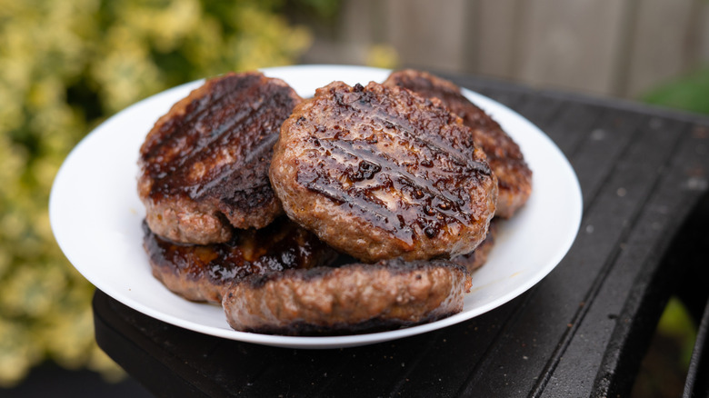 Pile of freshly grilled burgers on a white plate outdoors