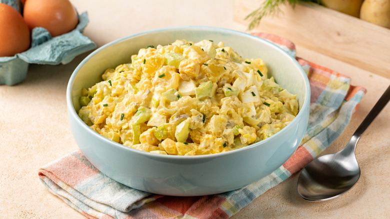 Bowl of creamy potato and egg salad next to a spoon