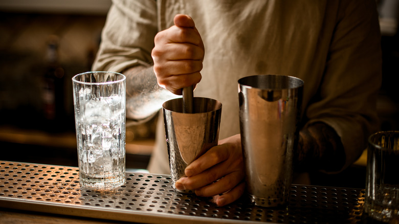 Bartender prepares a cocktail in a shaker using a muddler.