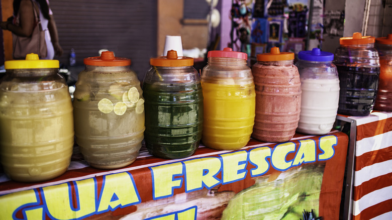 A variety of agua frescas in plastic containers on a table.