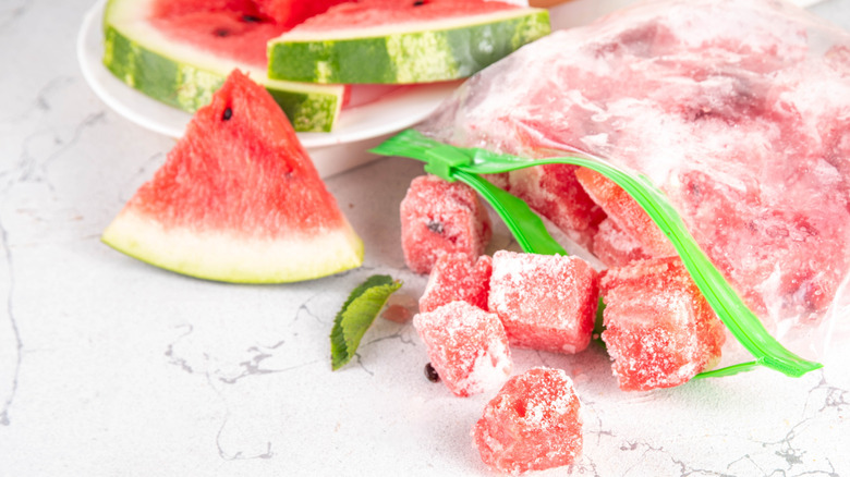 Frozen watermelon cubes in zip lock bag with watermelon slices in the background.