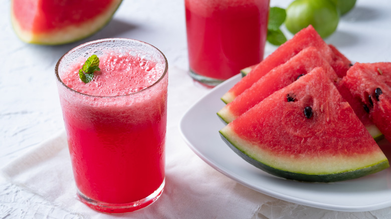 Glass of watermelon juice alongside watermelon slices on a white plate.