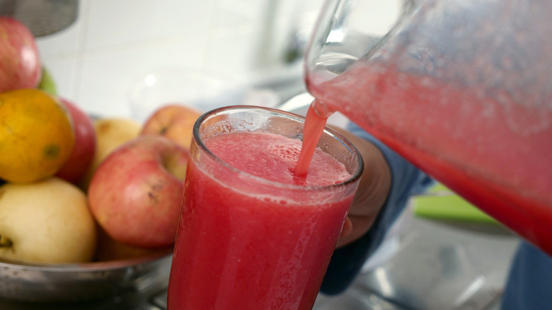 Watermelon puree being poured into glass with apples in background.