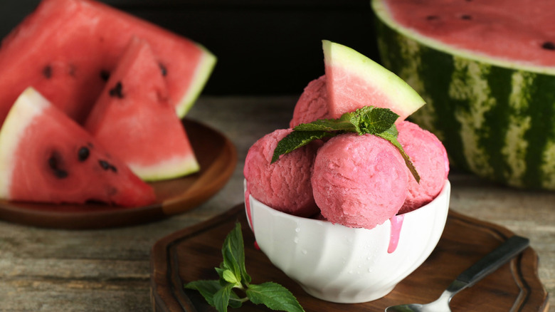 Scoops of watermelon sorbet in a white bowl with sliced watermelon in background.