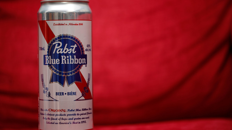 A can of Pabst Blue Ribbon beer against red curtain.