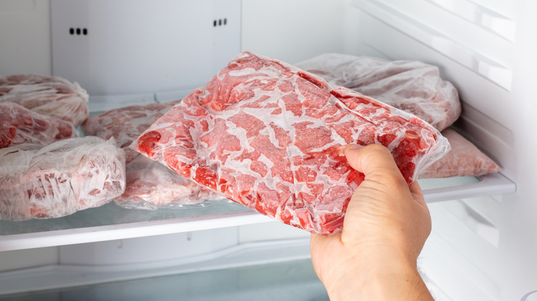A person grabs a package of meet from inside a freezer