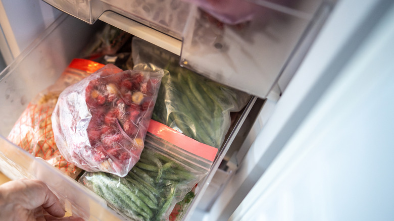 A person pulls out a drawer of frozen vegetables from the freezer