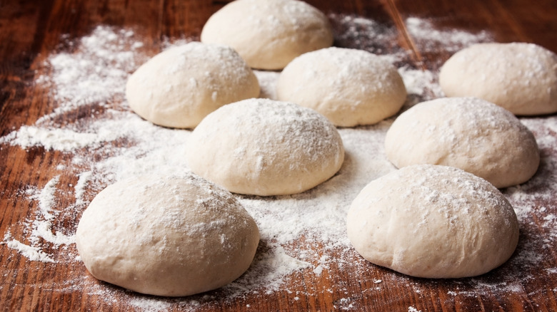 A wood plate with pizza dough balls on it