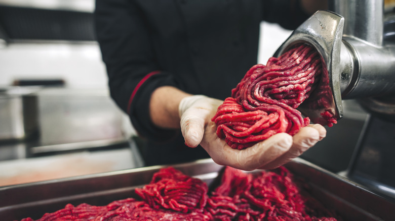 A chef grinds beef  into a large tray
