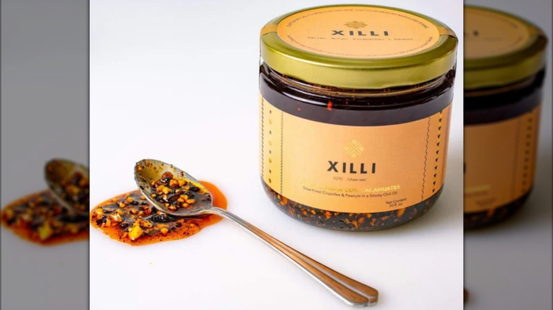 A jar of Xilli salsa macha beside a spoon with the sauce on it