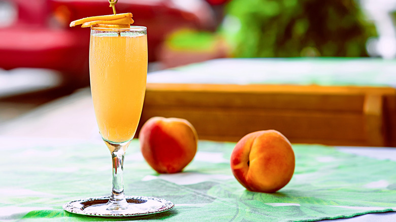 Peach bellini cocktail at an outdoor table with peaches beside it