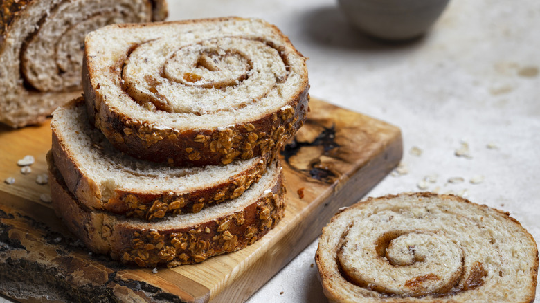 Slices of cinnamon swirl bread stacked on wooden board on stone surface