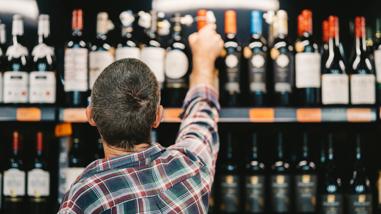 a man reaching for a wine bottle on shelf