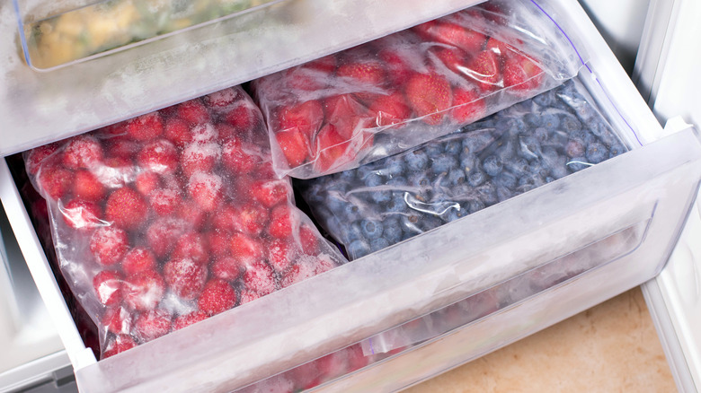 Bags of frozen strawberries and blueberries in a freezer drawer