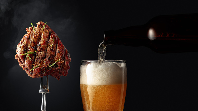 A piece of steak seasoned with pepper and rosemary held up on a fork next to a beer being poured into a glass