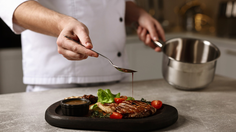 A chef's hand pours sauce over a steak with a spoon