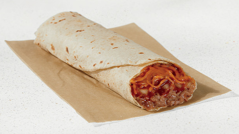 a Taco Bell bean burrito with the end chopped off laying on a brown piece of paper against a white background