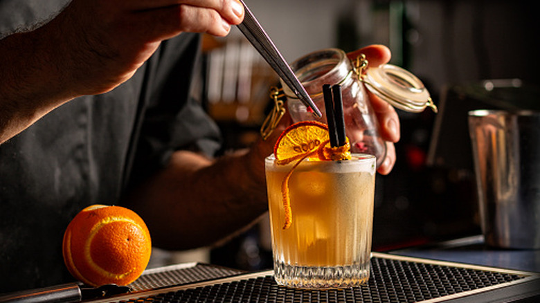 A bartender using tweezers to garnish a cocktail