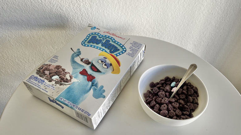 Boo Berry cereal in a white bowl next to a cereal box on a white table