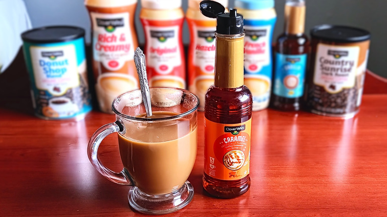 Glass mug with coffee and cream and spoon next to bottle of Clover Valley caramel syrup.
