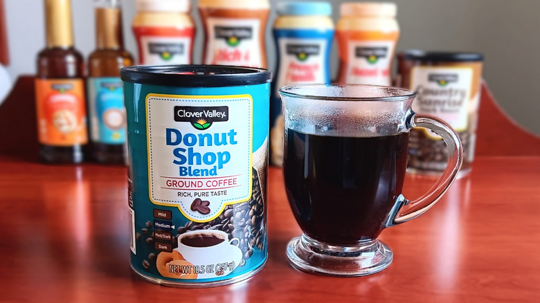 Clover Valley Donut Shop blend ground coffee next to a mug of black coffee.