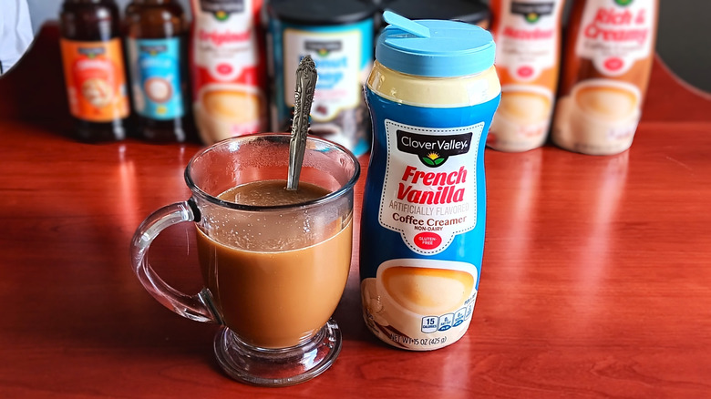 Glass mug of coffee with cream next to a container of Clover Valley French vanilla non-dairy coffee creamer.