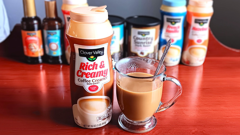 Container of Clover Valley Rich and Creamy non-dairy coffee creamer next to glass mug with coffee and cream.