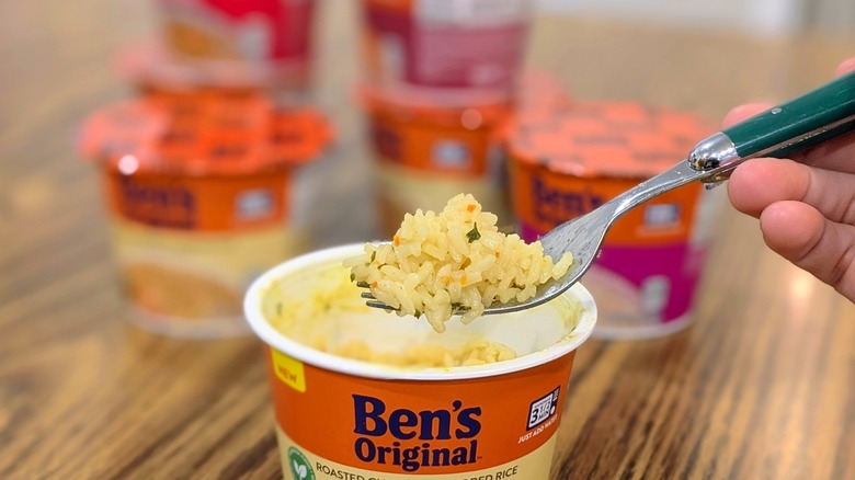A hand lifting some yellow rice out of a plastic cup with a fork with other cups of rice stacked in the blurry background