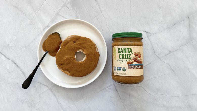 Peanut butter on a half of bagel with a jar of Santa Cruz peanut butter